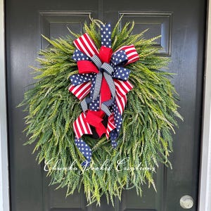 May include: A round, green wreath with a large bow featuring red, white, and blue ribbons. The bow has a patriotic design with American flag patterns and striped accents. The wreath is hanging on a black door.