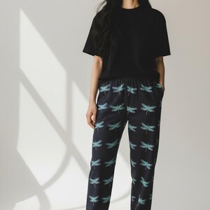 May include: Black short-sleeved t-shirt and navy blue pajama pants with a dragonfly pattern. The pants have an elastic waistband and a repeating pattern of teal dragonflies. The outfit is casual and comfortable.