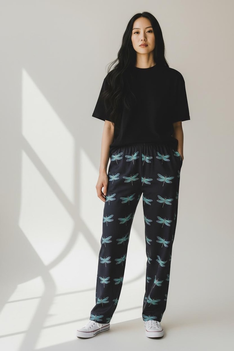 May include: Black short-sleeved t-shirt and navy blue pajama pants with a dragonfly pattern. The pants have an elastic waistband and a repeating pattern of teal dragonflies. The outfit is casual and comfortable.