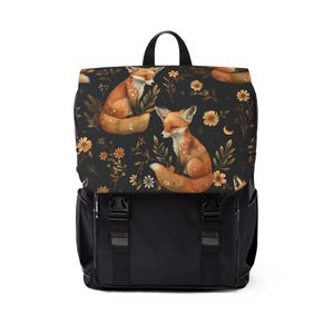 May include: A black backpack featuring a flap with a repeating pattern of orange foxes, yellow flowers, and small crescent moons. The bag includes a top handle, two black plastic buckle closures on the front, and side pockets with white stitching.