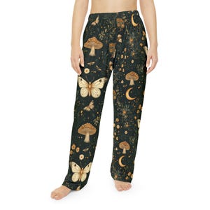 May include: Dark green pajama pants with a whimsical pattern of butterflies, mushrooms, moons, and flowers. The pants have a relaxed fit and a comfortable design, perfect for lounging or sleeping.