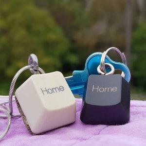 May include: Two keychains shaped like computer keys, both with the word "Home" printed on them. One keychain is white and the other is black.