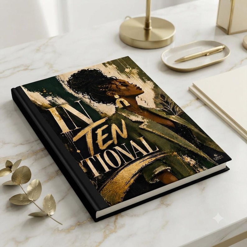 A closed hardcover journal with the Intentional cover design lies flat on a white marble desk beside a gold pen and small gold tray.