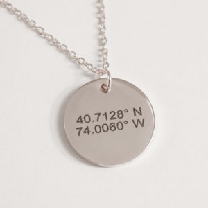 Puede incluir: Collar de plata con un colgante redondo grabado con las coordenadas 40.7128° N 74.0060° W.