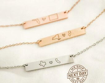 May include: Three gold bar necklaces with different state outlines and a heart. The necklaces are on a white surface. The bottom necklace has a "We Ship Next Day" stamp.