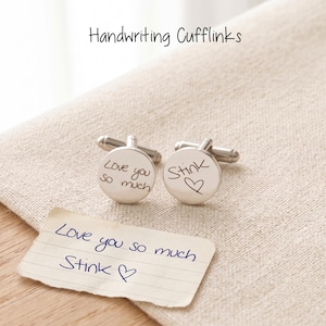 May include: A pair of round silver-toned metal cufflinks featuring custom black engraved handwriting. One cufflink displays the text Love you so much and the other displays the text Stink with a heart symbol, matching the handwritten note below.
