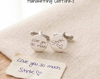 May include: A pair of round silver-toned metal cufflinks featuring custom black engraved handwriting. One cufflink displays the text Love you so much and the other displays the text Stink with a heart symbol, matching the handwritten note below.
