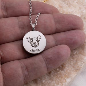 May include: Silver necklace with a round pendant featuring a black and white engraved image of a dog with the name "Charlie" engraved below.