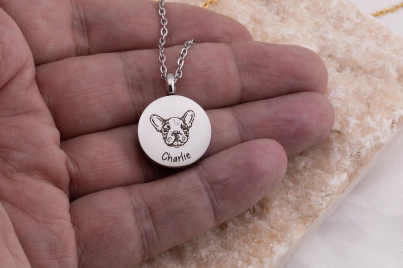 May include: Silver necklace with a round pendant featuring a black and white engraved image of a dog with the name "Charlie" engraved below.