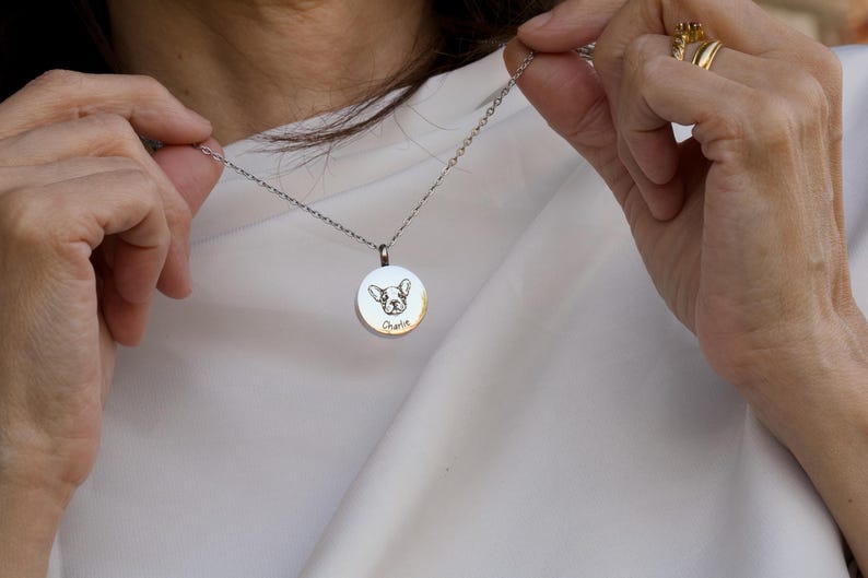 May include: A silver necklace with a round pendant featuring a dog's face and the name "Charlie" engraved on it.
