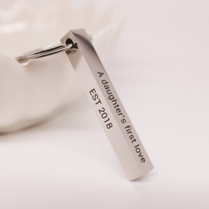 May include: Silver keychain with a rectangular charm that reads "A daughter's first love EST 2018".
