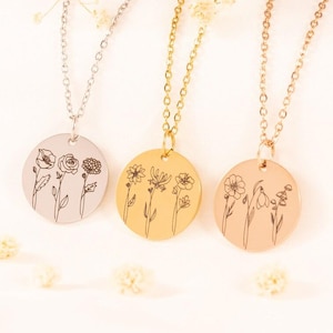 May include: Three circular pendant necklaces in silver, gold, and rose gold tones. Each pendant features a delicate black line art illustration of three different wildflowers. The necklaces are suspended from matching thin metal link chains.
