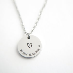 Puede incluir: Un collar de plata con un colgante redondo que presenta un corazón dibujado a mano y las coordenadas 29.7604° N, 95.3698° W.