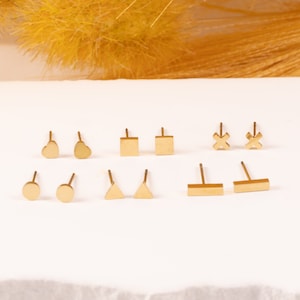 May include: A set of ten gold-toned stud earrings featuring different geometric shapes, including circles, squares, hearts, triangles, and an X.