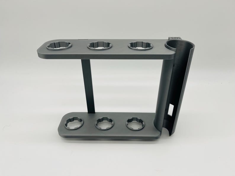 May include: A dark gray, multi-level stand with circular openings. The stand has a curved support on the right side and a rectangular base. The stand is designed to hold multiple items.