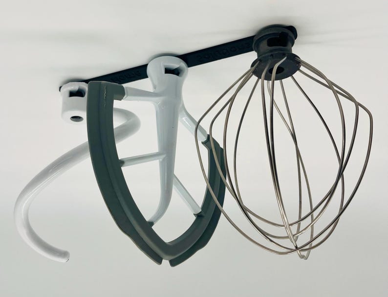 Op de afbeelding: Een verzameling opzetstukken voor een keukenmachine, waaronder een garde, een deeghaak en een platte klopper. De opzetstukken zijn in wit, grijs en zilver en zijn ontworpen voor diverse mengtaken in de keuken.