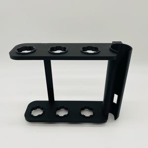 May include: A black 3D-printed stand with multiple circular openings and a cylindrical holder. The stand has a rectangular base with three openings and a top section with four openings. The design is modern and functional.