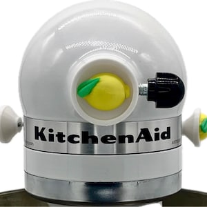 May include: White KitchenAid stand mixer with a lemon-shaped attachment and a black knob. The mixer has a silver band with the KitchenAid logo.