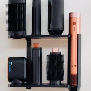 May include: A black and copper-colored hair styling tool set with multiple attachments, displayed on a black shelf. The set includes a curling wand, brushes, and a base unit. The text "Co-anda2x" is visible at the bottom.
