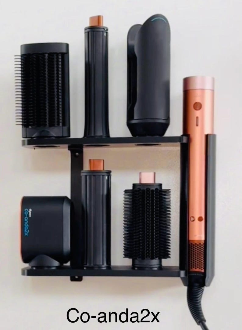 May include: A black and copper-colored hair styling tool set with multiple attachments, displayed on a black shelf. The set includes a curling wand, brushes, and a base unit. The text "Co-anda2x" is visible at the bottom.