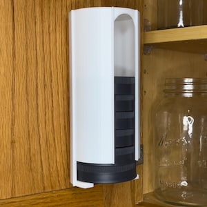 Peut inclure: Un conteneur de rangement en plastique blanc avec une porte coulissante, monté sur une porte d'armoire en bois. Le conteneur contient cinq boîtes en plastique noir.