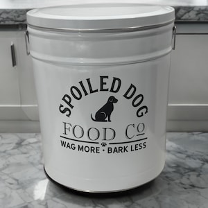以下が含まれることがあります： 「Spoiled Dog Food Co. Wag More Bark Less」と犬のシルエットが描かれた白黒のロゴがついた白い金属製の犬用フードコンテナです。