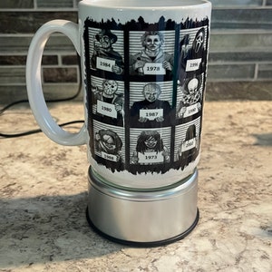 Pode incluir: Caneca de cerâmica branca com uma imagem em preto e branco de personagens de filmes de terror em fotos de ficha policial. Cada ficha policial tem um ano impresso abaixo do personagem. A caneca está em um descanso de copo prateado.