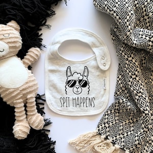 May include: White baby bib with a black and white llama wearing sunglasses and the text "Spit Happens".