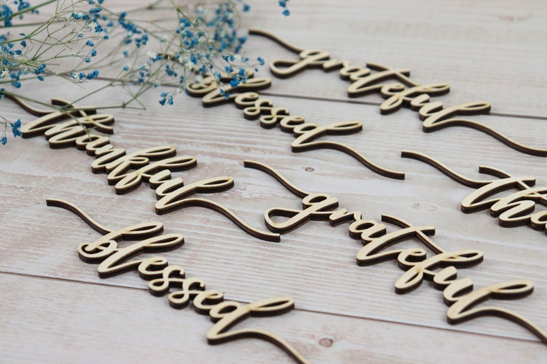 Puede incluir: Palabras recortadas de madera con las palabras "thankful", "blessed", "grateful" y "thankful" en una fuente cursiva. Las palabras est&aacute;n dispuestas en un patr&oacute;n escalonado sobre una superficie de madera clara.