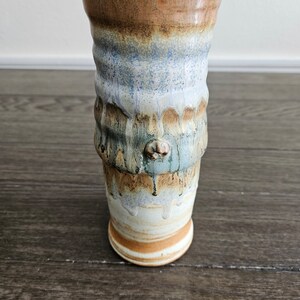 May include: A ceramic vase with a textured, wavy design. The vase is glazed in shades of brown, blue, and white.