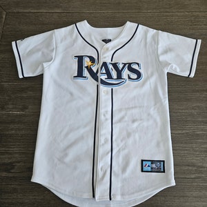 May include: White baseball jersey with blue and yellow "Rays" logo and black piping. The jersey has a button-up front and a tag on the bottom right side.