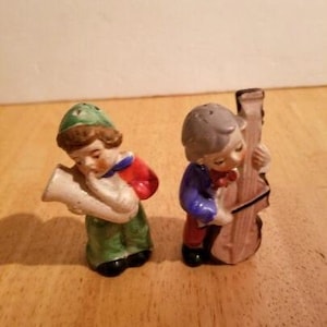 May include: A pair of vintage ceramic salt and pepper shakers. One figure is dressed in green, red, and white, playing a horn. The other figure, in blue and red, plays a string bass. Both figures have gray hair and black shoes.