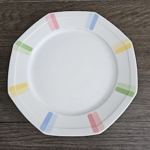 May include: White octagonal dinner plate with a colorful striped design around the edge. The stripes are pink, blue, yellow, and green.