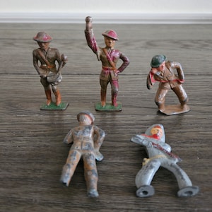 May include: Five vintage toy soldiers made of painted metal. The soldiers are wearing different uniforms and hats. Some of the soldiers are holding weapons or musical instruments.