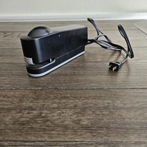 May include: A black electric stapler with a cord and plug. The stapler has a silver trim and a black button on the top.