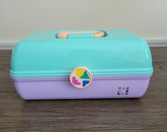 May include: A teal and purple plastic storage box with a geometric design on the latch. The box has a handle on the top and the text "CAB LLE" on the front.