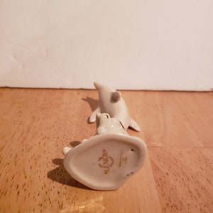 May include: White porcelain figurine of two dolphins, one leaping over the other. The figurine is made by Lenox and has a gold inscription on the base.