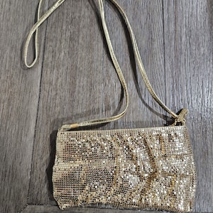 May include: A gold chainmail crossbody bag with a long strap. The bag is made of small, linked metal squares.