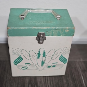 May include: Vintage vinyl record storage box. The box is white with a teal green lid and handle. The front of the box features a teal green design of records and musical notes. The box has a metal clasp closure.