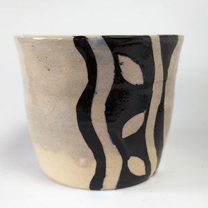 Puede incluir: Una maceta de cerámica con un esmalte blanco y rayas negras pintadas y formas de hojas.