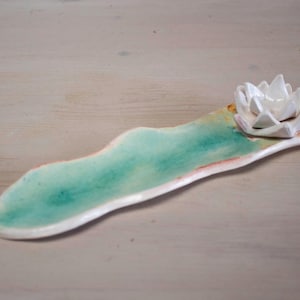 Puede incluir: Porta incienso de cerámica blanca con forma de flor de loto sobre una base en forma de hoja verde y blanca.