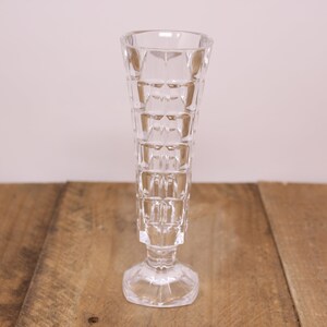 May include: A clear glass vase with a geometric pattern. The vase has a wide base and a narrow neck.