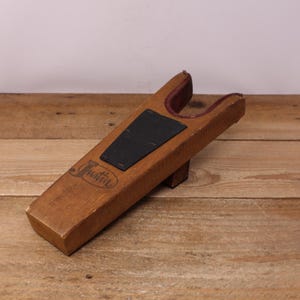 May include: A wooden boot jack with a dark brown finish. The boot jack has a black rubber grip and a burgundy-colored interior. The word "Justin" is printed on the side of the boot jack.