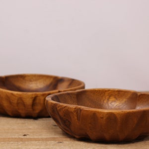 May include: Two wooden bowls with a carved design. The bowls are brown and have a natural wood finish.