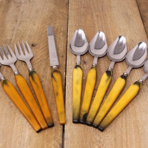 May include: A set of vintage silverware with yellow and black plastic handles. The set includes four forks, a knife, and five spoons.
