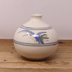 May include: A white ceramic vase with a round body and a narrow neck. The vase is decorated with blue, green, and brown brushstrokes in a stylised floral pattern.