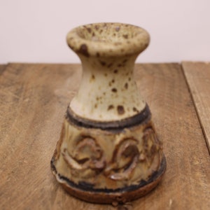 Peut inclure: Un petit bougeoir en céramique blanche avec des mouchetures brunes et un motif décoratif autour de la base.