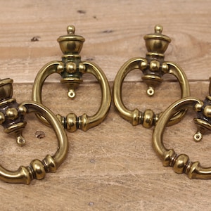 May include: Four antique brass cabinet knobs with a ring pull and ornate design. The knobs have a rounded top and a decorative base.