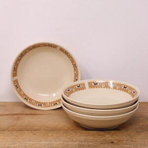 May include: A set of four cream-coloured ceramic bowls featuring a brown geometric border pattern with repeating horse motifs along the inner rim. One bowl is positioned upright to the left, while three bowls are stacked neatly on the right side.