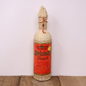 May include: A vintage wicker-wrapped bottle of Bristol's Muscatel wine. The label is red with gold lettering and features a crown and the text "Bodegas La Silla".